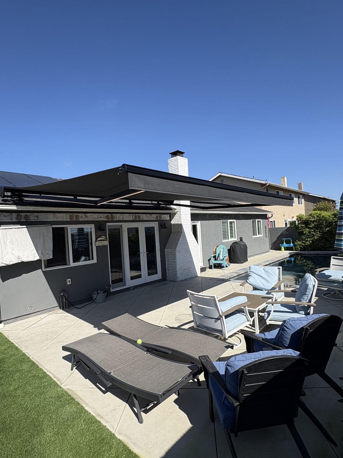 Black cassette retractable awning extended over a poolside patio, installed by AJ Shades